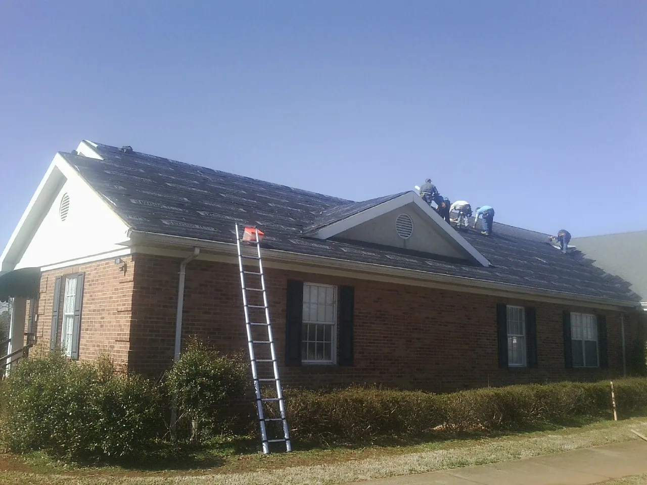 Crew tearing shingles off a brick ranch roof with a ladder set — Emergency Roof Repair work by our crew in Harwood Heights
