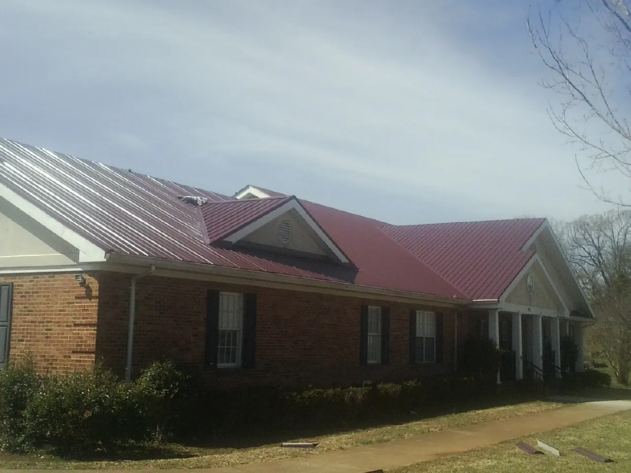 Red metal roof with gabled entries on a long brick building, from a Hail Damage Roof Repair job in Harwood Heights