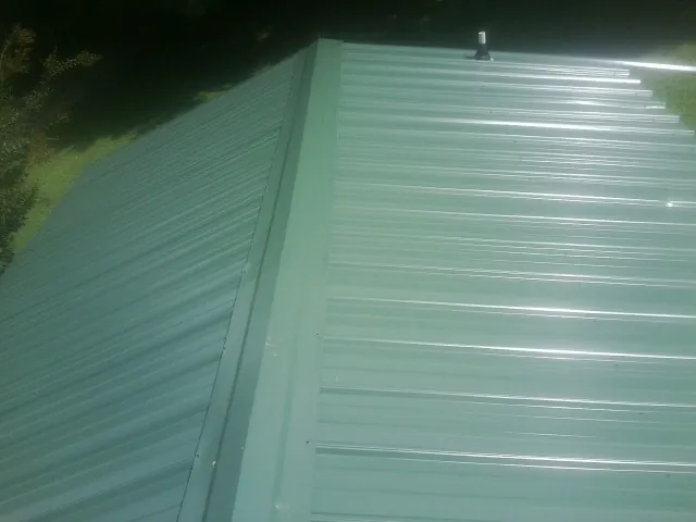 New green metal panels meeting at the ridge of a roof — Flat Roof Repair work by our crew in Harwood Heights