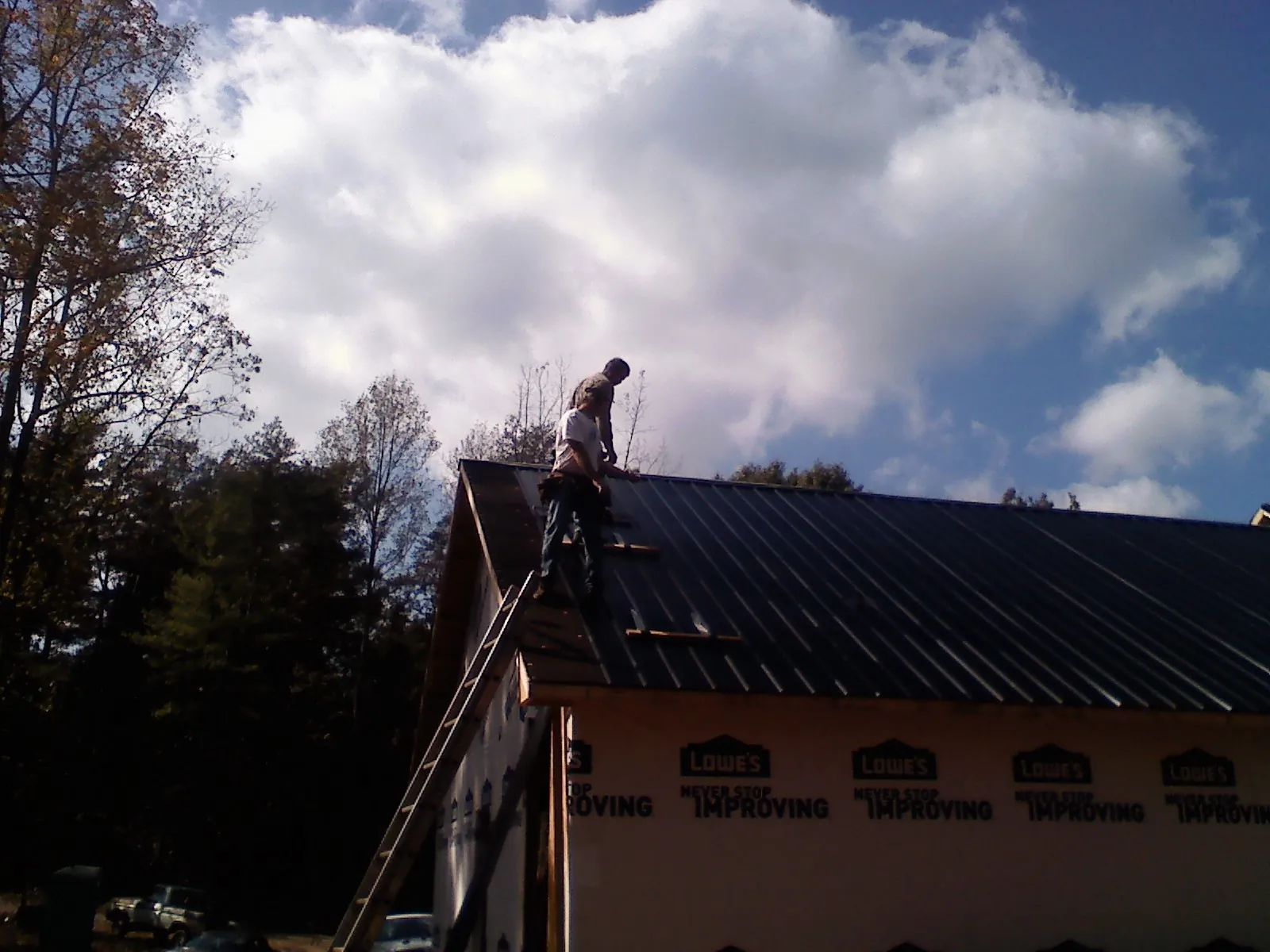 Roofer fastening dark metal panels high against a cloudy sky, from a Roof Inspection job in Harwood Heights