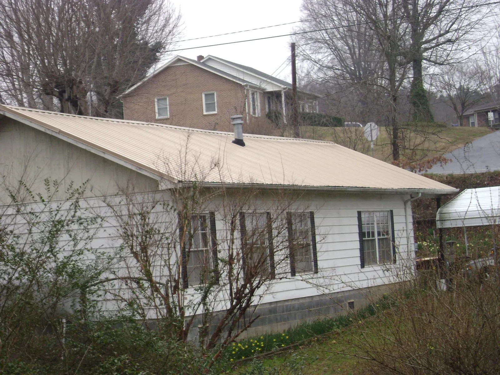 Tan metal roof on a white sided house set into a hillside — Commercial Roofing by Roofing Brothers in Harwood Heights